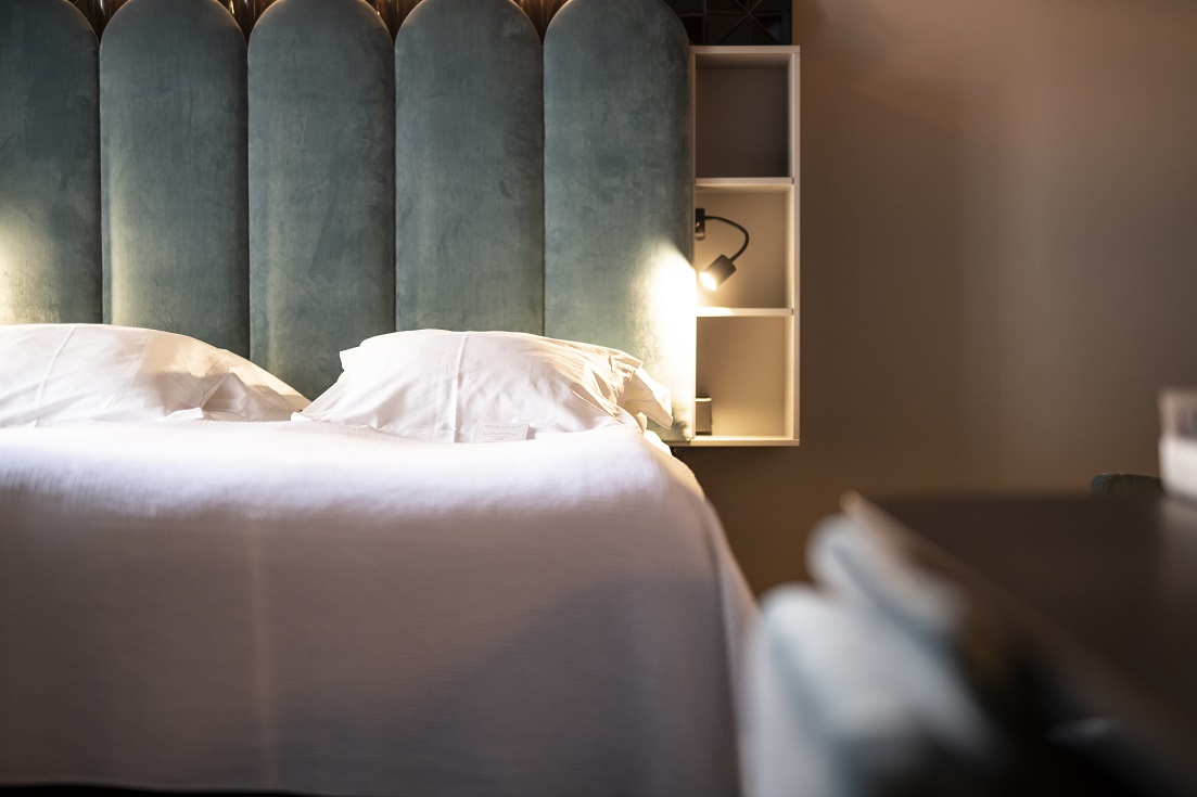 Hotel Flora room — teal velvet headboard and warm bedside lighting