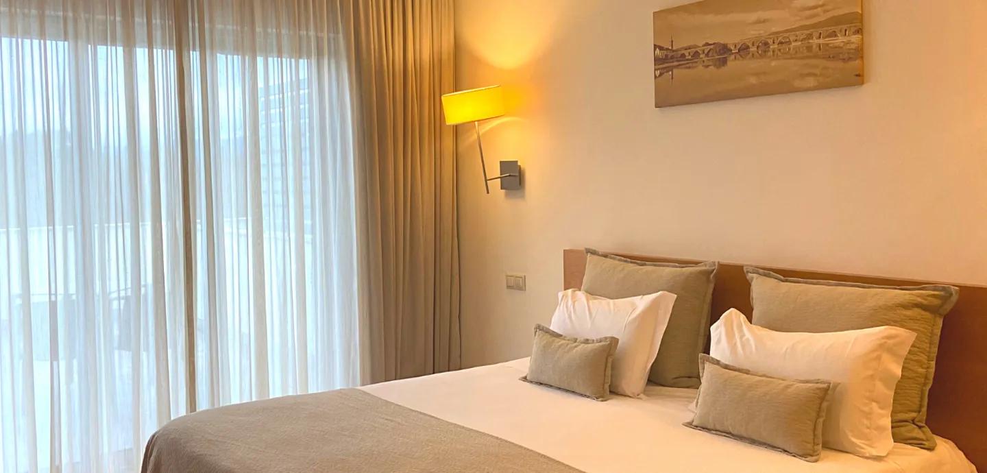 Minho hotel room — warm lamp, green linen and painting of Roman bridge