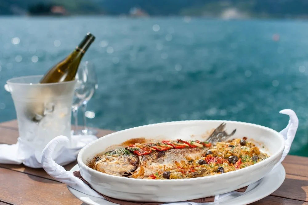Baked fish with olives and peppers, white wine on ice — waterfront dining in Perast
