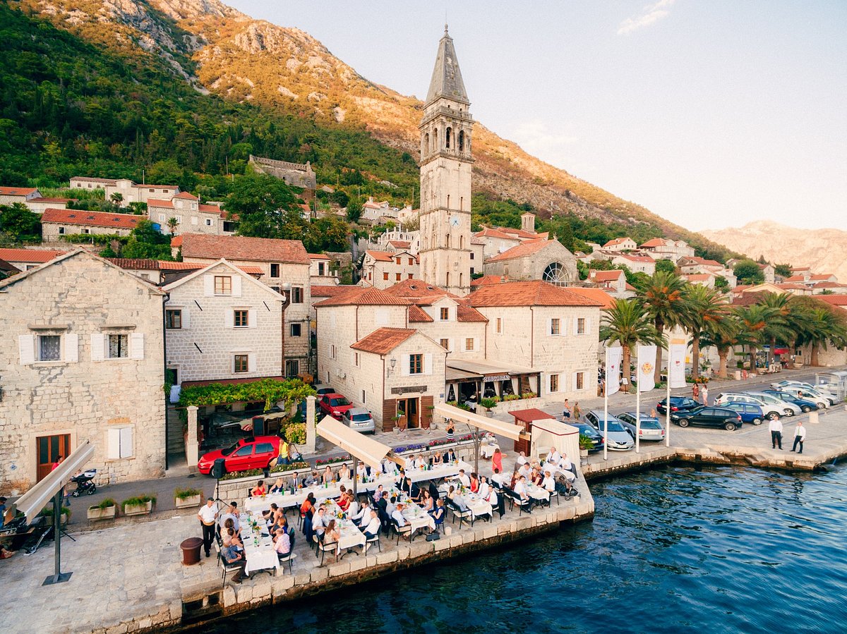 Perast waterfront dining at golden hour — St Nicholas bell tower and honey limestone palaces